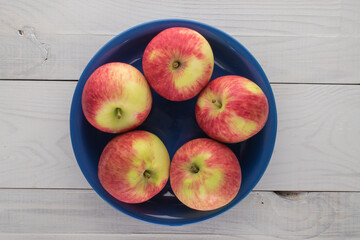 Several ripe apples in a ceramic plate on a wooden table, top view.