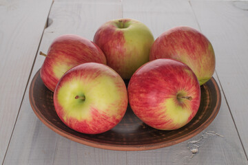 Several ripe apples in a ceramic plate on a wooden table