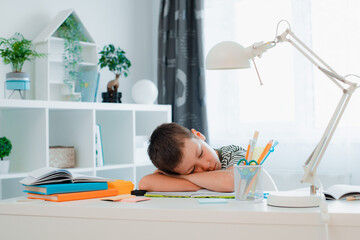 Tired schoolboy sleeping on his table after completing a home school assignment. Back to school