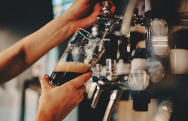 woman bartender hand at beer tap pouring a dark beer in glass serving in a restaurant or pub - obrazy, fototapety, plakaty