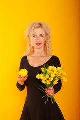 blonde girl on a yellow background with yellow bouquets of tulips and lemon in her hands