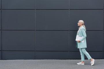Side view of senior businesswoman with newspaper walking near building outdoors