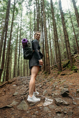 young woman hiking in the woods with a backpack and a mat