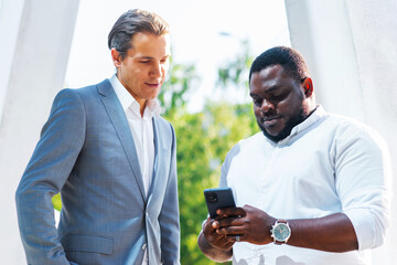 African-American businessman and his colleague in front of modern office building. Financial investors are talking outdoor. Banking and business concept.