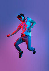 Fototapeta na wymiar Stylish young asian man jumping isolated over lilac color studio background in pink neon light. Concept of human emotions, fashion, beauty, youth