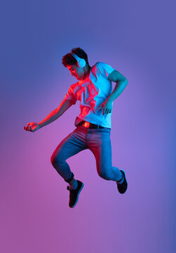 Stylish Young Asian Man Jumping Isolated Over Lilac Color Studio Background In Pink Neon Light. Concept Of Human Emotions, Fashion, Beauty, Youth