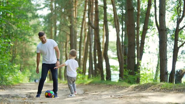 Father and son playing football soccer in the woods or park on an outdoor lawn. dad and little boy have fun together sport in nature Forest camp parent and kid play ball. Family weekend. Fathers day