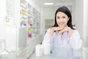 asian female pharmacist rest in drugstore, she feeling happy and smile, she rest chin on her hand