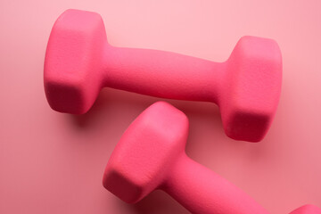 Two pink female dumbbells isolated on pink background close-up with copy space. Fitness concept, weight loss and sport activity, top view, flat lay