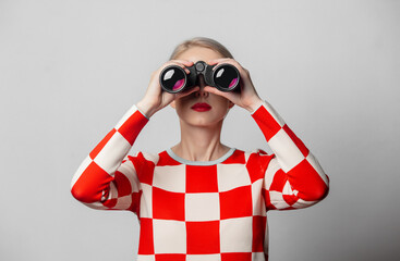 Beautiful woman with blond hair in in a 70s red square dress with binocular