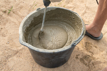 Mixing cement mortar in a bucket with an electric construction drill close-up