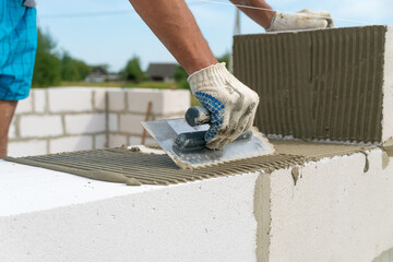Builder uses a notched trowel to apply the cement mixture to the sides of the building block....