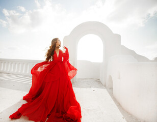 Fashion outdoor photo of gorgeous young woman with red hair in airy red dress posing on the streets...