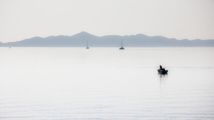fisher boat on the smooth sea in the morning with mountains in the background