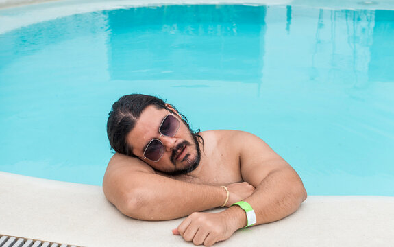 An overweight man dozes off at the side of the swimming pool. Exhausted or bored vacationer.