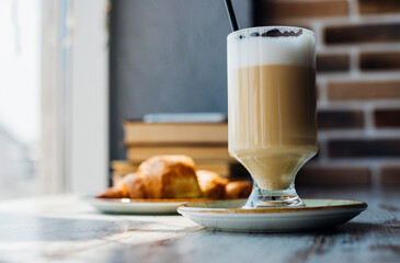 Latte in a tall glass against the background of a stack of books. The drink is on the table in a cafe.