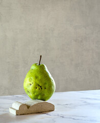 A large fresh pear stands on a marble stand, balancing. The concept is a balance of fresh fruits. Copying space, minimalism..