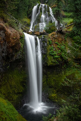 View of a two-tier waterfall in Oregon. Falls creek falls can be seen with cascading water and green moss in a lush forest. 