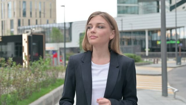Serious Young Businesswoman Walking on the Street while Looking Around 