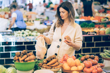 Middle age stylish pregnant woman enjoy shoping, holding reusable cotton shopping net bag in eco friendly farmer market. Zero waste concept. New alternative.