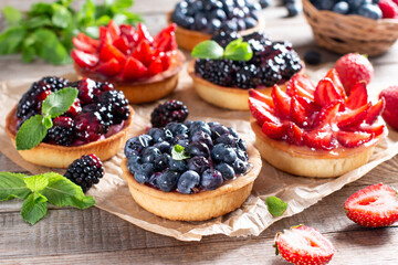 Strawberries, blueberries, blackberries tartlets with chocolate ganache, fresh berries and mint leaves. Fresh fruit tart, freshly homemade fruit cake on a table