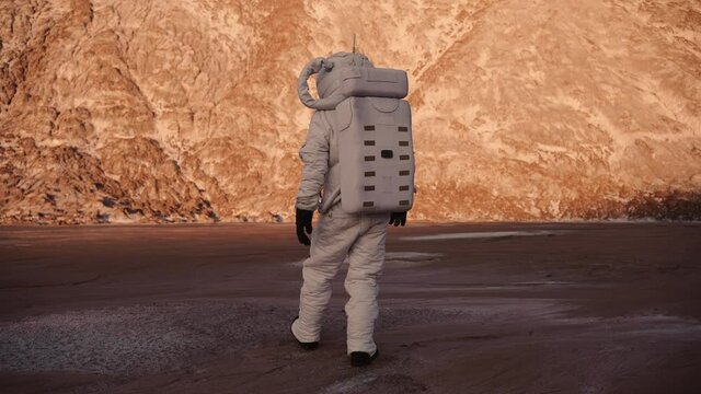 male astronaut is walking on an unknown planet. the sun is shining. discovery of a new planet. astronaut walking towards the hill