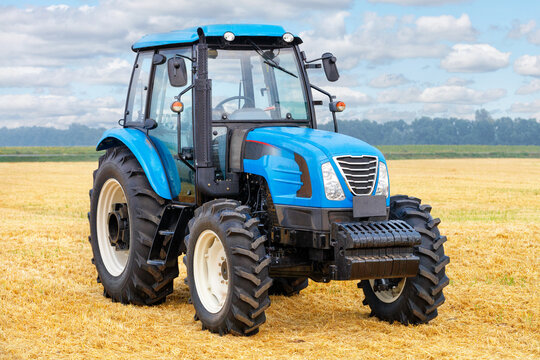 Fototapeta Wheeled farm tractor with harvested yellow wheat field and cloudy sky in the background.