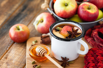 Homemade hot fruit tea with fresh apples, honey, spices: cinnamon, cardamon, anise, clove. Warm autumn drink, delicious healthy beverage. Mulled wine. Cozy fall home atmosphere. Wooden background