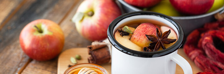 Homemade hot fruit tea with fresh apples, honey, spices: cinnamon, cardamon, anise, clove. Warm autumn drink, delicious healthy beverage. Mulled wine. Cozy home atmosphere. Wooden background. Banner