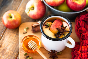 Homemade hot fruit tea with fresh apples, honey, spices: cinnamon, cardamon, anise, clove. Warm autumn drink, delicious healthy beverage. Mulled wine. Cozy fall home atmosphere. Wooden background