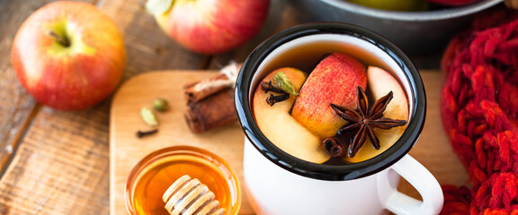 Homemade hot fruit tea with fresh apples, honey, spices: cinnamon, cardamon, anise, clove. Warm autumn drink, delicious healthy beverage. Mulled wine. Cozy home atmosphere. Wooden background. Banner