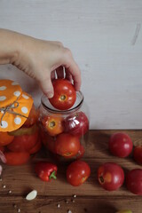 The hand puts red tomatoes in a jar and spices on the table.