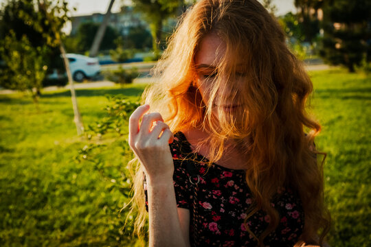 Thoughtful redhead lady wind swept hair covering her face with closed eyes, backlit by summer sun. Summertime alone mood
