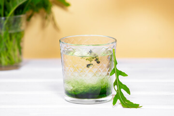 Green Chlorophyll drink in glass with water on white table, Orange Background. Green Drops in clear water, Antioxidant food and drinks.