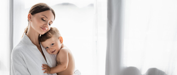 pleased mother in bathrobe holding in arms nude toddler son, banner