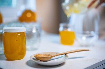 Someone pours honey into transparent jars on a white table