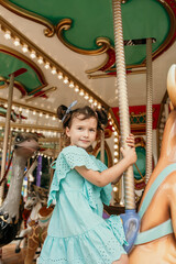 a little girl in a blue dress rides on an attraction in an amusement park