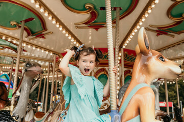Fototapeta na wymiar funny little girl in a blue dress rides on an amusement park ride