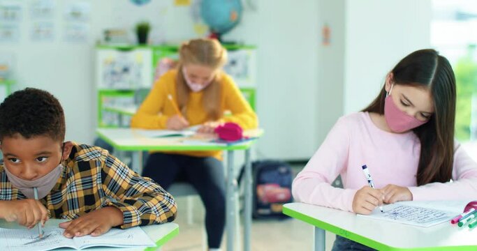 Close up of multi-ethnic diverse school children sitting in classroom writing in copybook with pencil, studying, education learning concept Male and female junior students sitting at desk in classroom