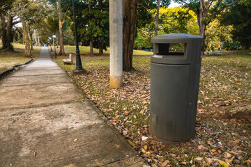 Trash can in a natural park on the side of the road, surrounded by trees.