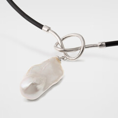 Closeup of silver necklace with pretzel loop and uncut pearl pendant on gray background
