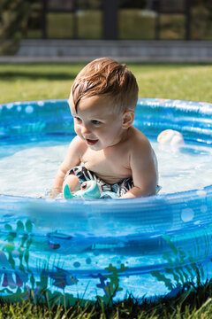 cheerful toddler boy sitting in inflatable pool with rubber toys