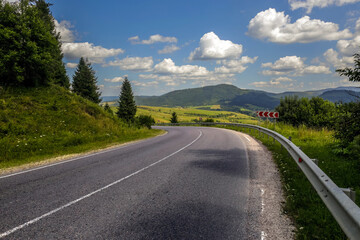 Asphalt road in mountain hilly countryside in pine forests, on background of blue sky with clouds, Ukraine, Carpathians