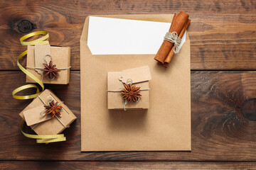 Fototapeta na wymiar Paper gift boxes with anise on envelope with cinnamon at the brown wooden background. Eco friendly package for presents on New Year and Christmas