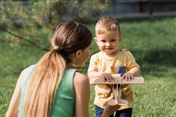 mother looking at toddler boy with wooden biplane outside
