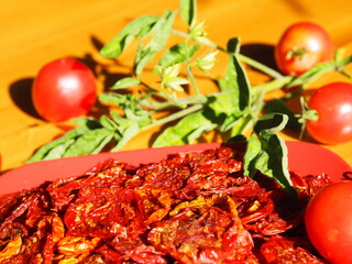 Sun-dried tomatoes in a red plate on a wooden table. Evening sun. Horizontal format. Close-up.