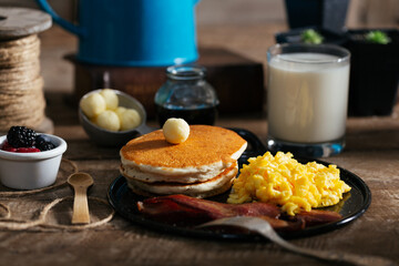 Pancake stack, eggs, bacon, syrup, milk, cup of fruit