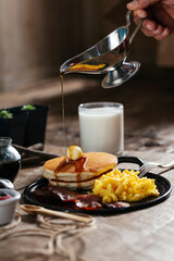 Pancake stack, eggs, bacon, syrup, milk, cup of fruit