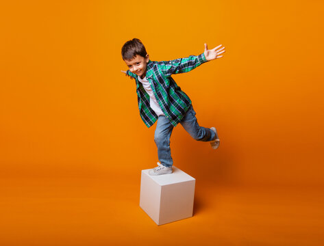 happy little boy smiling and holding balance, standing on one leg on a cube in the studio.