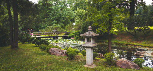 a japanese garden with a bridge and a sculpture - obrazy, fototapety, plakaty